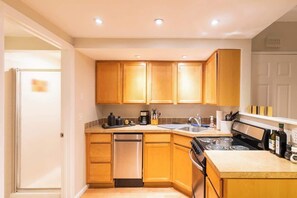 A compact kitchen with wooden cabinets, a dishwasher, a stove, and a sink. - Chic Downtown Denver Retreat | Walk Everywhere + Stylish Comfort (Denver)
