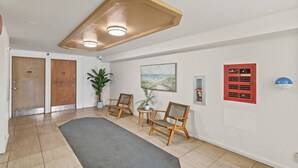 A hallway with two wooden doors, a potted plant, a painting, a red fire safety panel, and a blue smoke detector. - Skyline Access w/ Pearl Views - W/D, Parking, A/C (Pearl City)