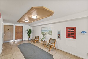 Un pasillo con dos puertas de madera, una planta en maceta, un cuadro, un panel rojo de seguridad contra incendios y un detector de humo azul.