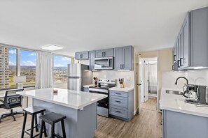 Una cocina moderna con armarios grises, una isla central y vistas a un paisaje urbano a través de grandes ventanales.