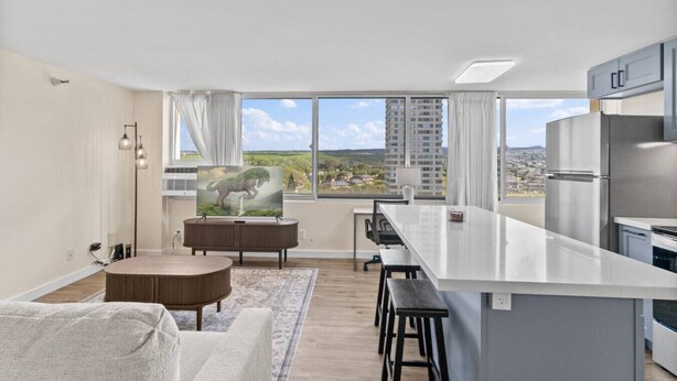 A modern apartment with a kitchen, dining area, and a large window with a city view. - Skyline Access w/ Pearl Views - W/D, Parking, A/C (Pearl City)