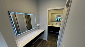 A bathroom with a vanity, a mirror with LED lighting, a shower area, and a dark wood floor. - Modern Ground Floor Studio w/ Patio & Kitchen (Freeport)