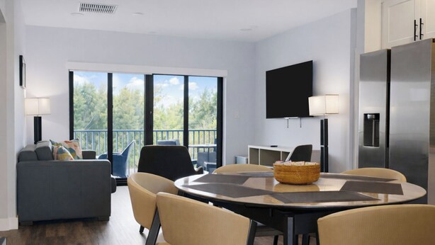 Una sala de estar moderna con comedor, ventanas amplias, televisor de pantalla plana y refrigerador.