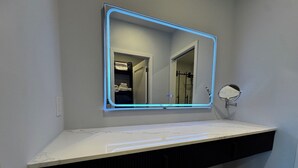 Ett badrum med ett vitt handfat, en spegel med blått LED-ljus och en handdukshängare.