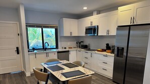A modern kitchen with white cabinets, a stainless steel refrigerator, a microwave, and a dining area with a marble table and chairs. - Relaxing 1-Bedroom Suite w/ Balcony & Sleeps 4 (Freeport)