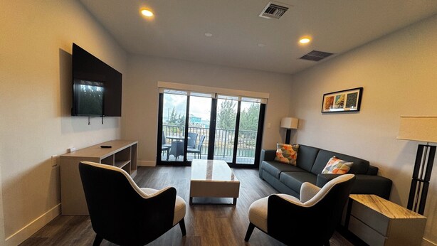 Una sala de estar moderna con un televisor de pantalla plana, un sofá, dos sillones, una mesa de centro y un ventanal corredizo que da a un área exterior.