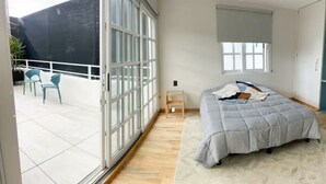 Una camera da letto con un letto, un comodino, una finestra e un balcone con sedie.