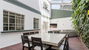 Zona pranzo esterna moderna con tavolo e sedie bianche, un molo in legno e un muro verde con piante.