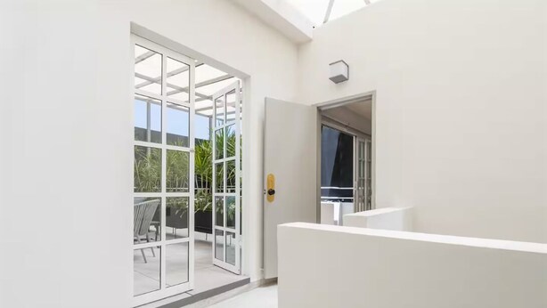 Un interno moderno con una porta in vetro che dà su un'area esterna, una parete bianca e un soffitto con lucernari.