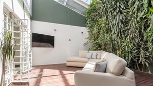 Un interno moderno con un divano beige, una TV bianca montata a parete e una parete verde ricoperta di piante.