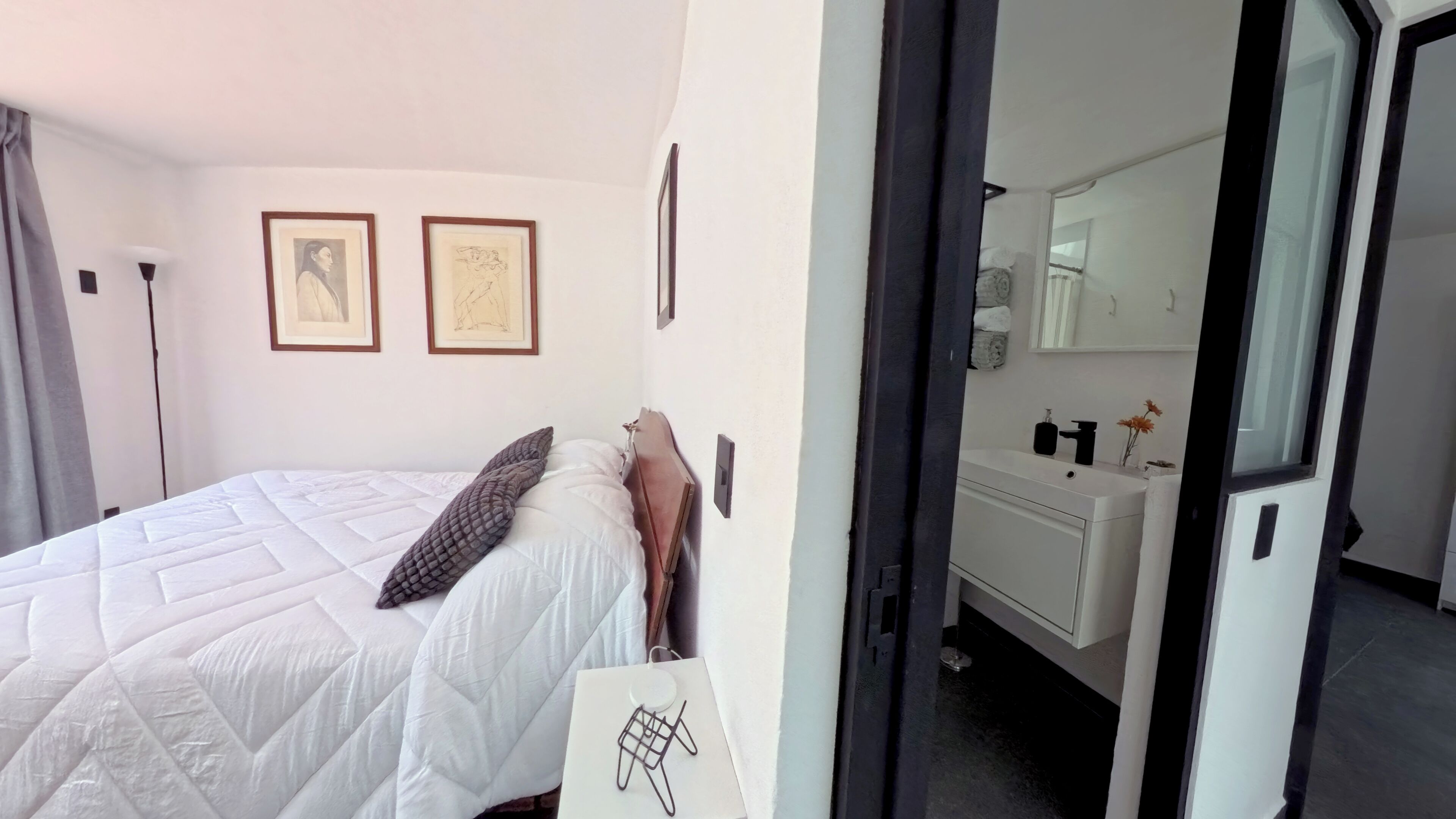 Ein Schlafzimmer mit Bett, Nachttisch, Fenster und einer Tür zu einem Badezimmer.