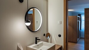 A modern bathroom with a wooden vanity, a round mirror, and a wall-mounted light fixture. - Münsterhus Josefs Alpine Lodge - Zimba four-bed room (Schruns)