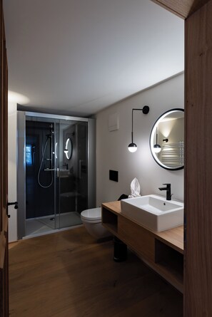 A modern bathroom with a glass-enclosed shower, a white sink, and a round mirror. - Münsterhus Josefs Alpine Lodge - Zimba four-bed room (Schruns)