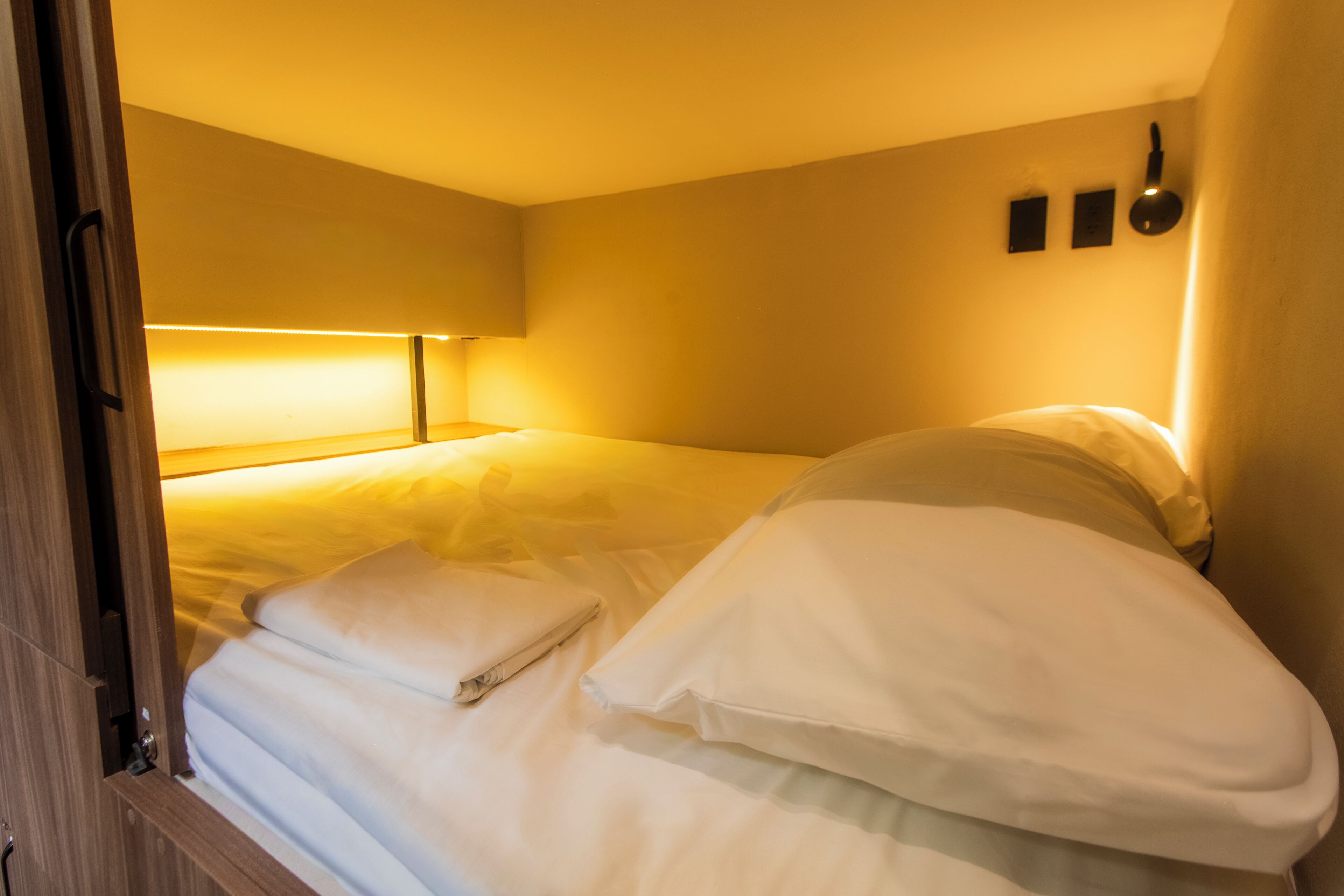Una habitación de hotel con cama, mesita de noche y lámpara de pared.