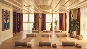 Una habitación amplia con piso de madera, ventanas grandes con cortinas y varias plantas en macetas.