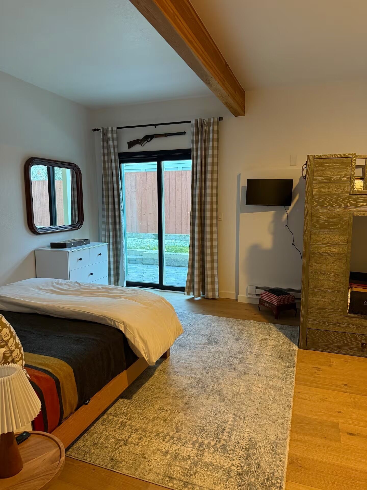 Une chambre à coucher avec un lit, une télévision, une fenêtre avec des rideaux, un plafond en bois et une petite table avec une lampe.