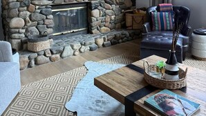 Ein Wohnzimmer mit Kamin aus Stein, einem darüber montierten Fernseher und einer Couch mit Kissen.