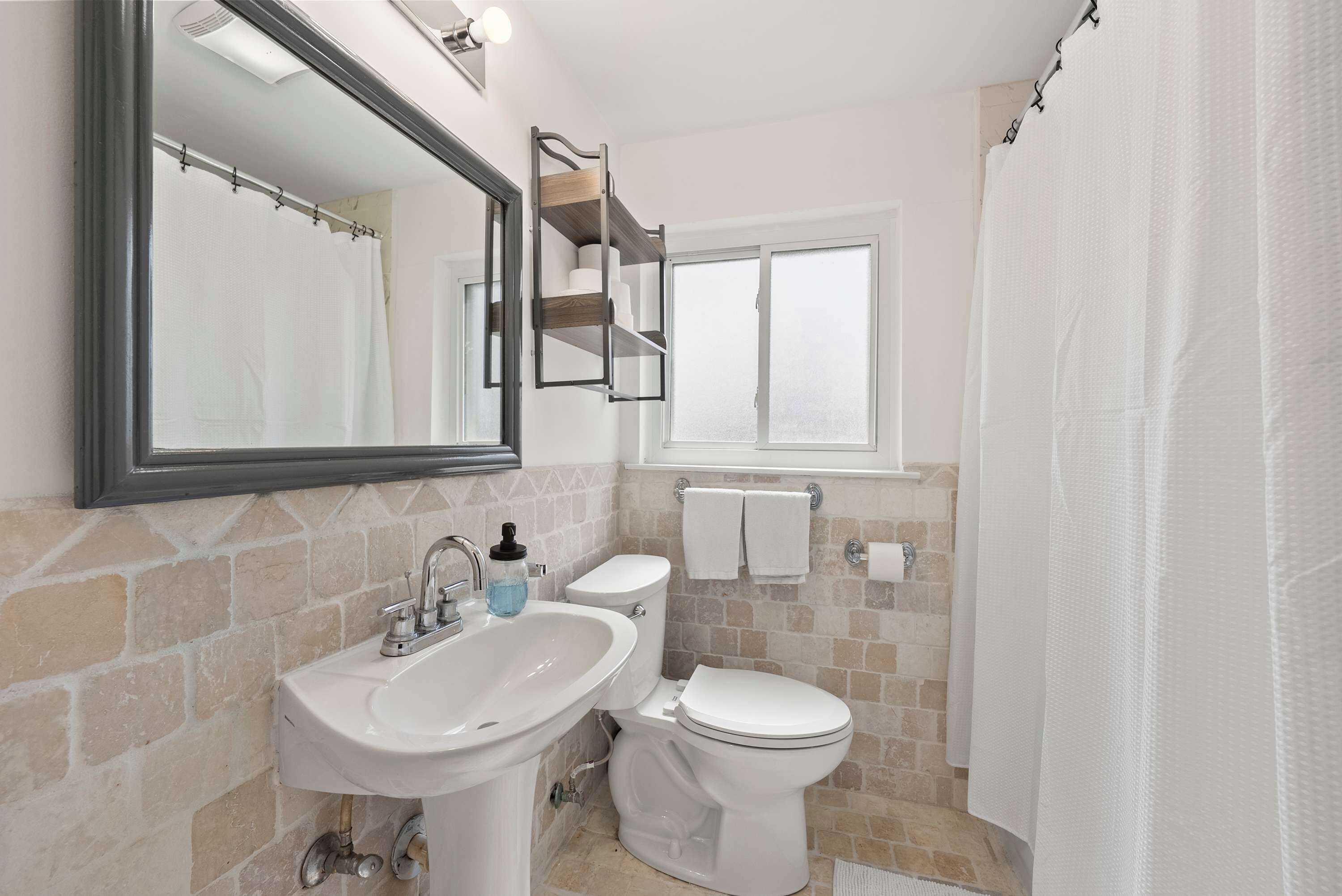 A bathroom with a sink, mirror, toilet, and shower curtain.