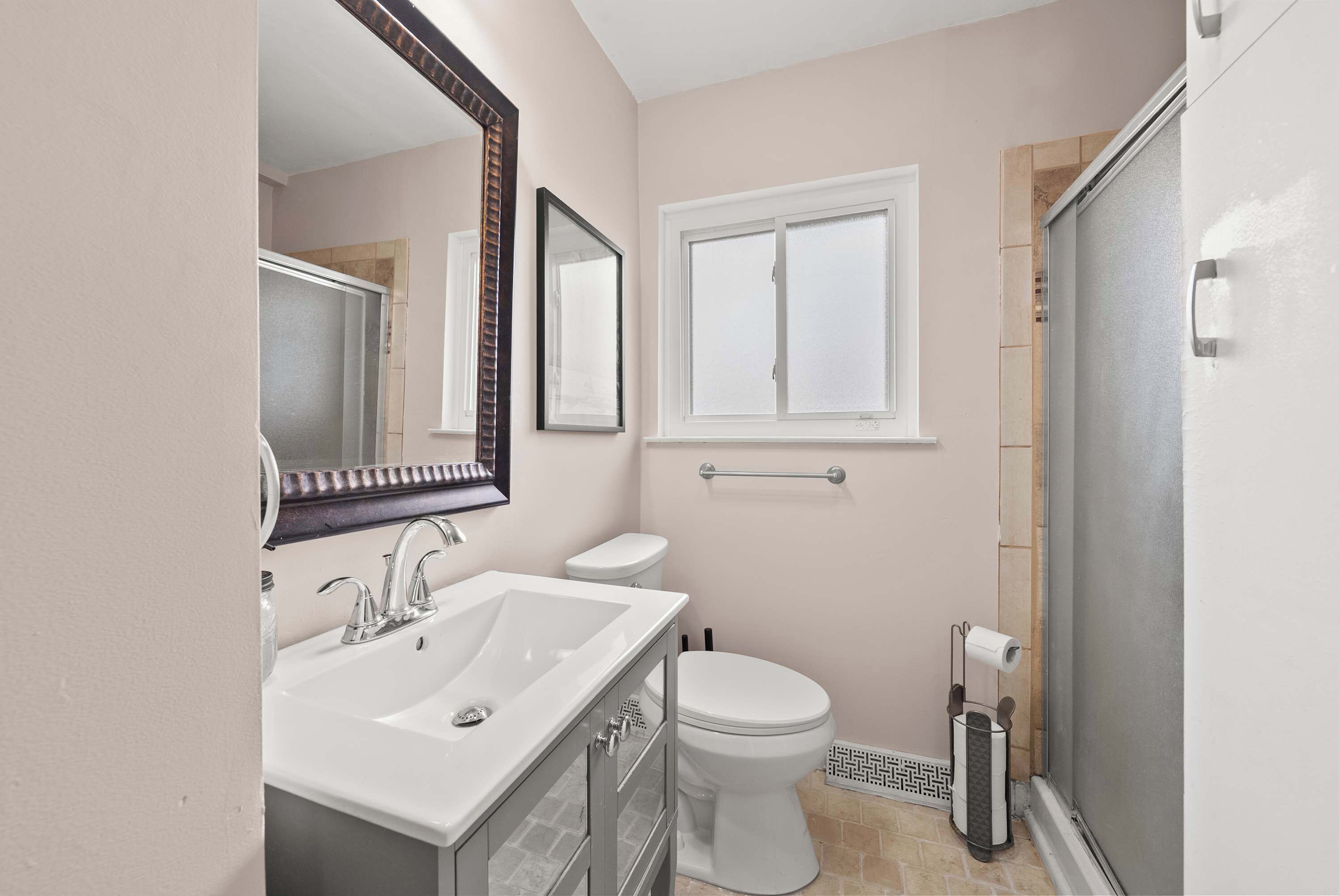 A bathroom with a white sink, a toilet, a shower, and a window.