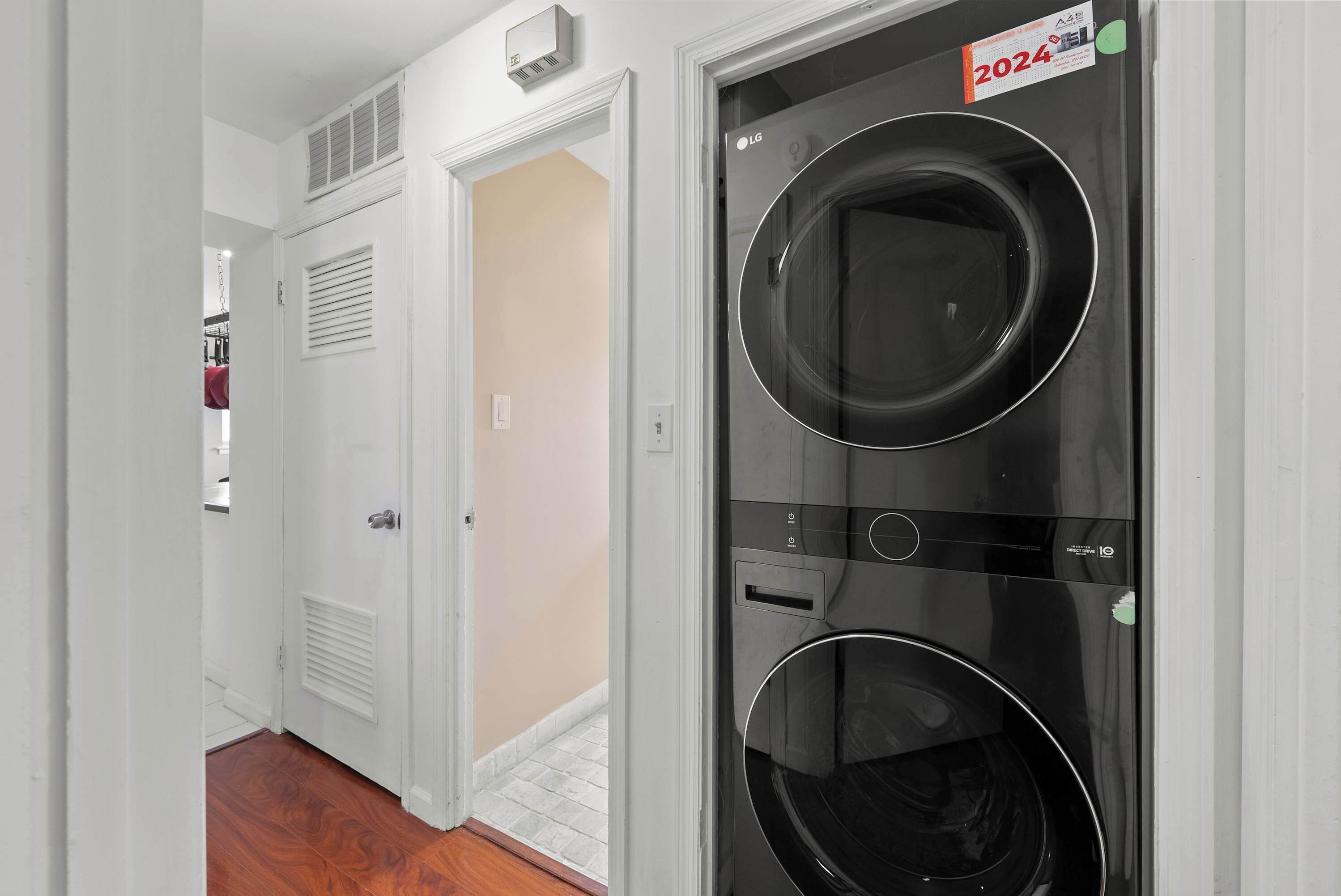 A laundry room with two black washing machines, a white door, and a vent on the wall.