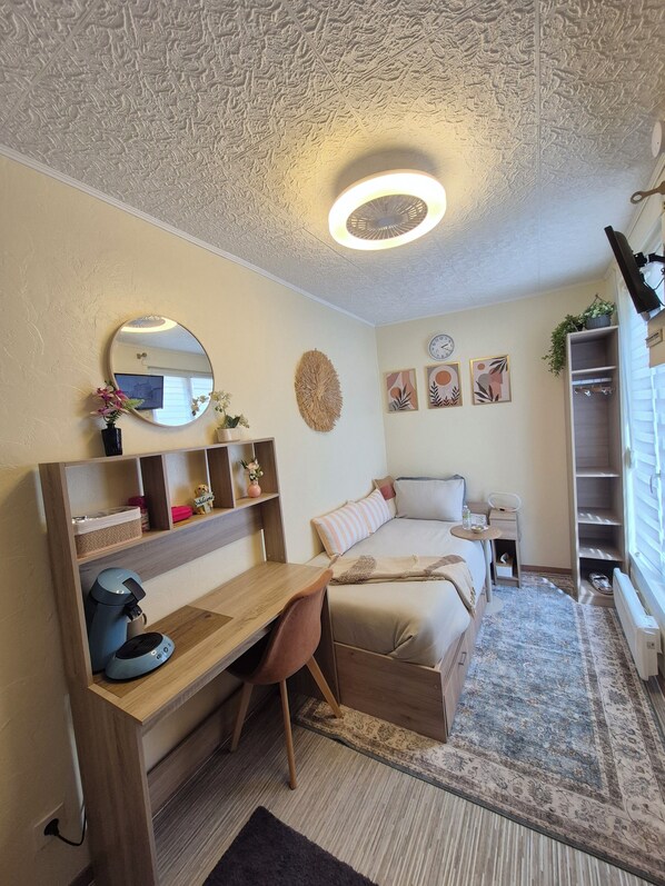 Un dormitorio con una cama, un escritorio, una silla, un espejo redondo, un reloj y una estantería decorada.