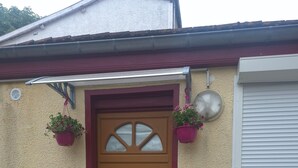 A brown door with a window, a red door frame, a welcome mat, and two hanging flower pots. - Independent studio (Châlons-en-Champagne)
