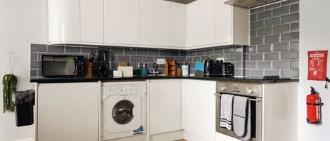 A compact kitchen with a microwave, washing machine, oven, and a fire extinguisher.