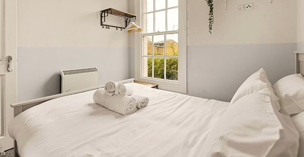 Ein ordentlich bezogenes Bett mit aufgerollten Handtüchern, einem Heizkörper und einem Fenster mit Blick auf Grünflächen.