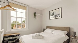 Ein Schlafzimmer mit Bett, Fenster, Nachttisch, Lampe und einem an der Wand befestigten Regal mit einer Pflanze.
