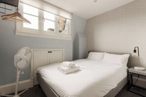 Ein Schlafzimmer mit einem Bett, einem Nachttisch, einem Wandventilator, einem Fenster mit Blick und einer Pendelleuchte.
