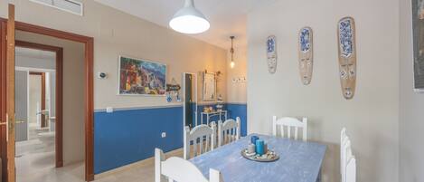 Un coin repas avec une table bleue, des chaises blanches et un luminaire suspendu.