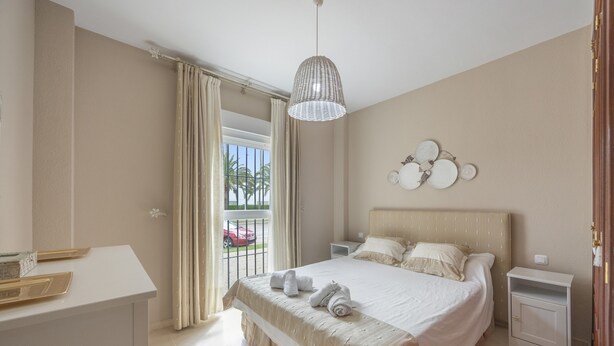 Habitación de hotel con cama, mesitas de noche, escritorio y balcón con cortinas.
