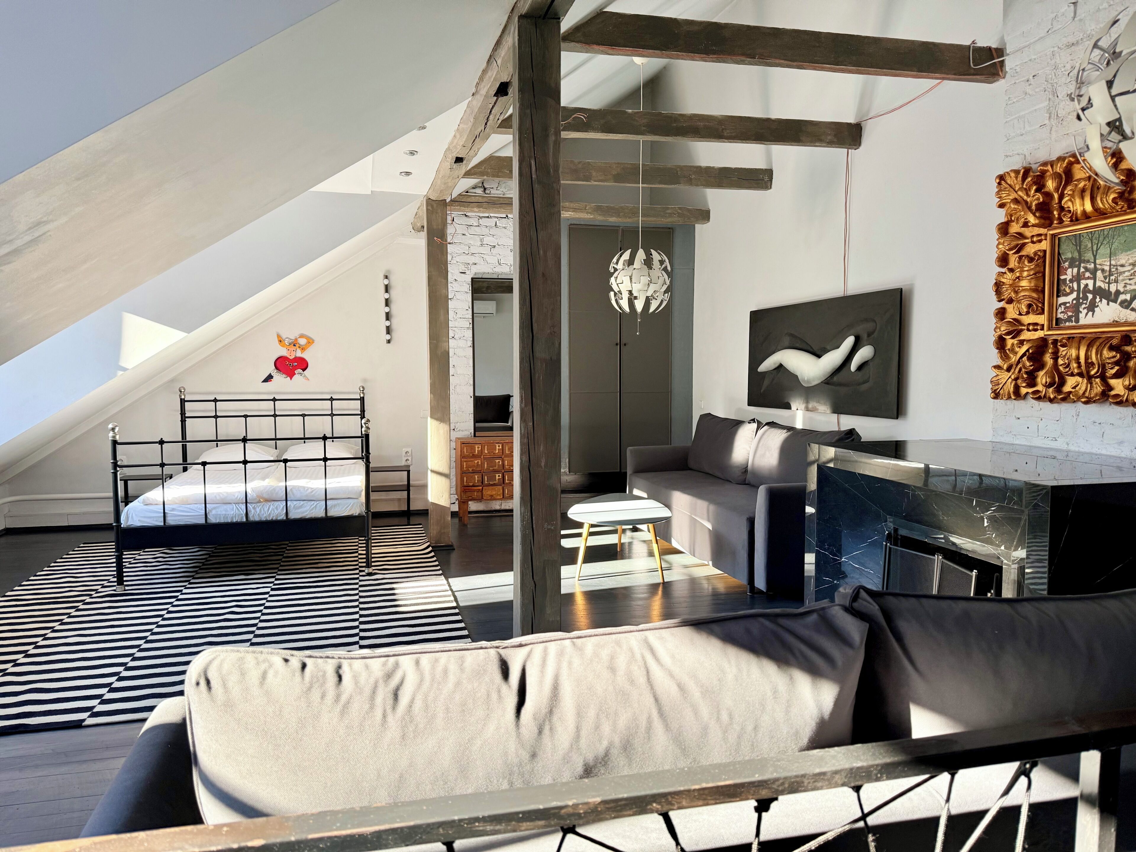 Ein modernes Schlafzimmer im Loft-Stil mit schrägem Dach, einem Bett, einer Couch, einem kleinen Tisch und einem Kamin.
