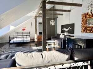 A modern loft bedroom with a sloped ceiling, a bed, a sofa, a fireplace, and a large window.