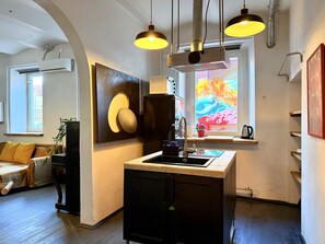 Une cuisine moderne dotée d’un îlot central, de luminaires suspendus et d’une fenêtre offrant une vue colorée.