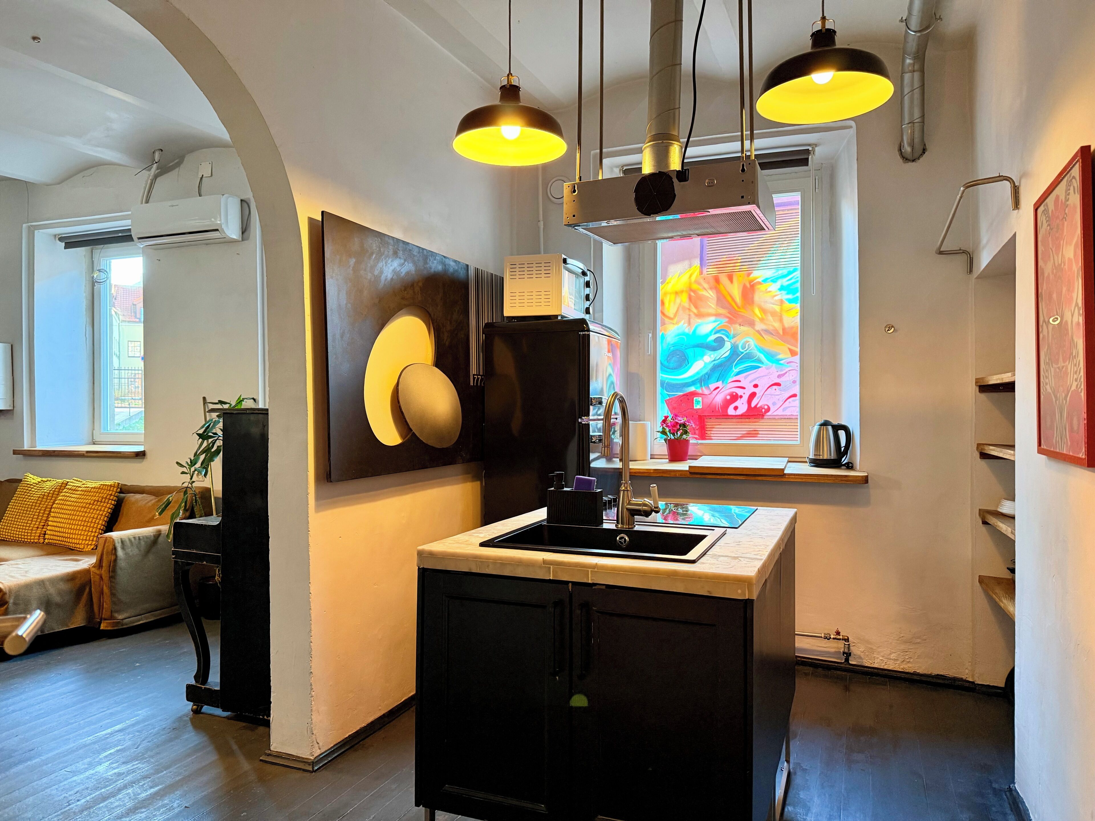 A modern kitchen with a central island, pendant lighting, and a colorful window view.