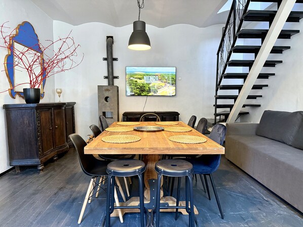 A dining area with a wooden table, black chairs, a black pendant light, a television displaying 'MEXICO,' and a staircase.