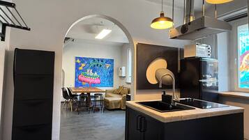 A modern kitchen with a central island, a dining area with chairs, a sofa, and a colorful painting on the wall.
