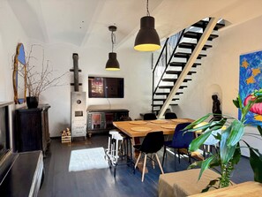 A modern interior with a wooden dining table, black chairs, a staircase, and a TV mounted on the wall. - Uzupio2 Old Town Studio (Vilnius)