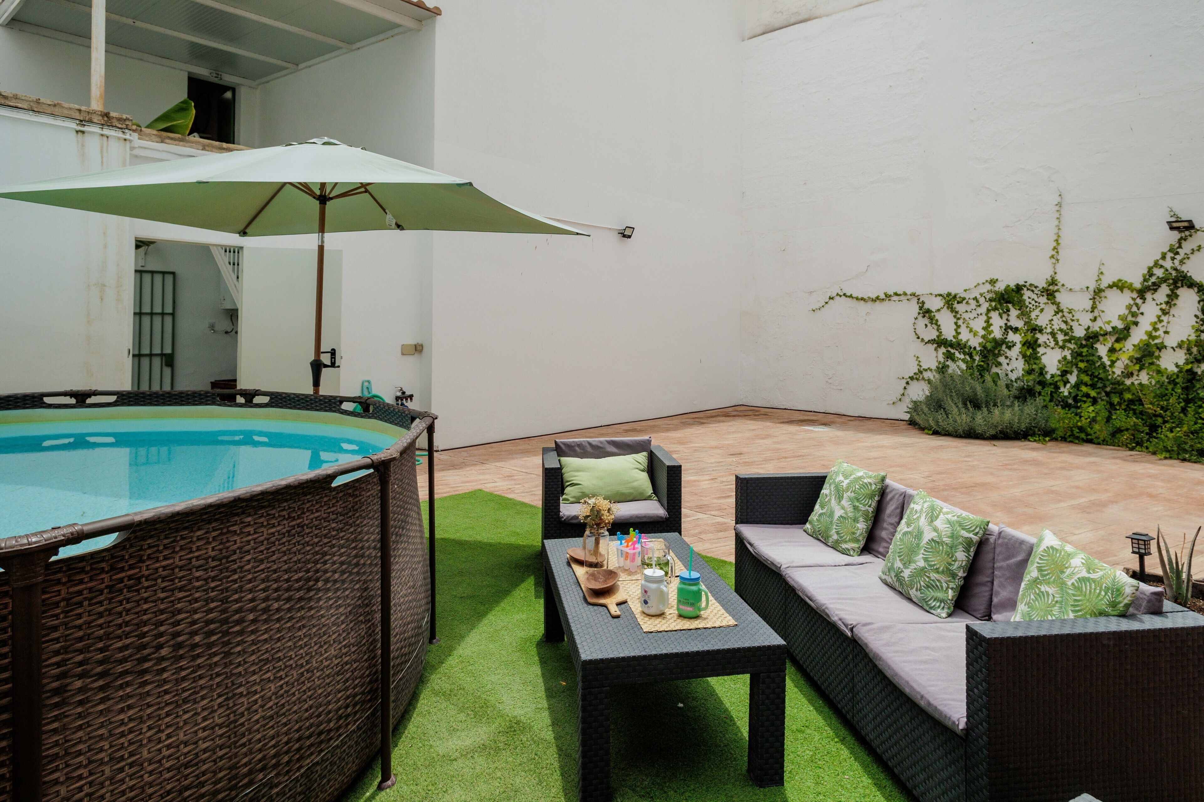 Une terrasse avec un jacuzzi, des meubles en osier et un parasol vert.