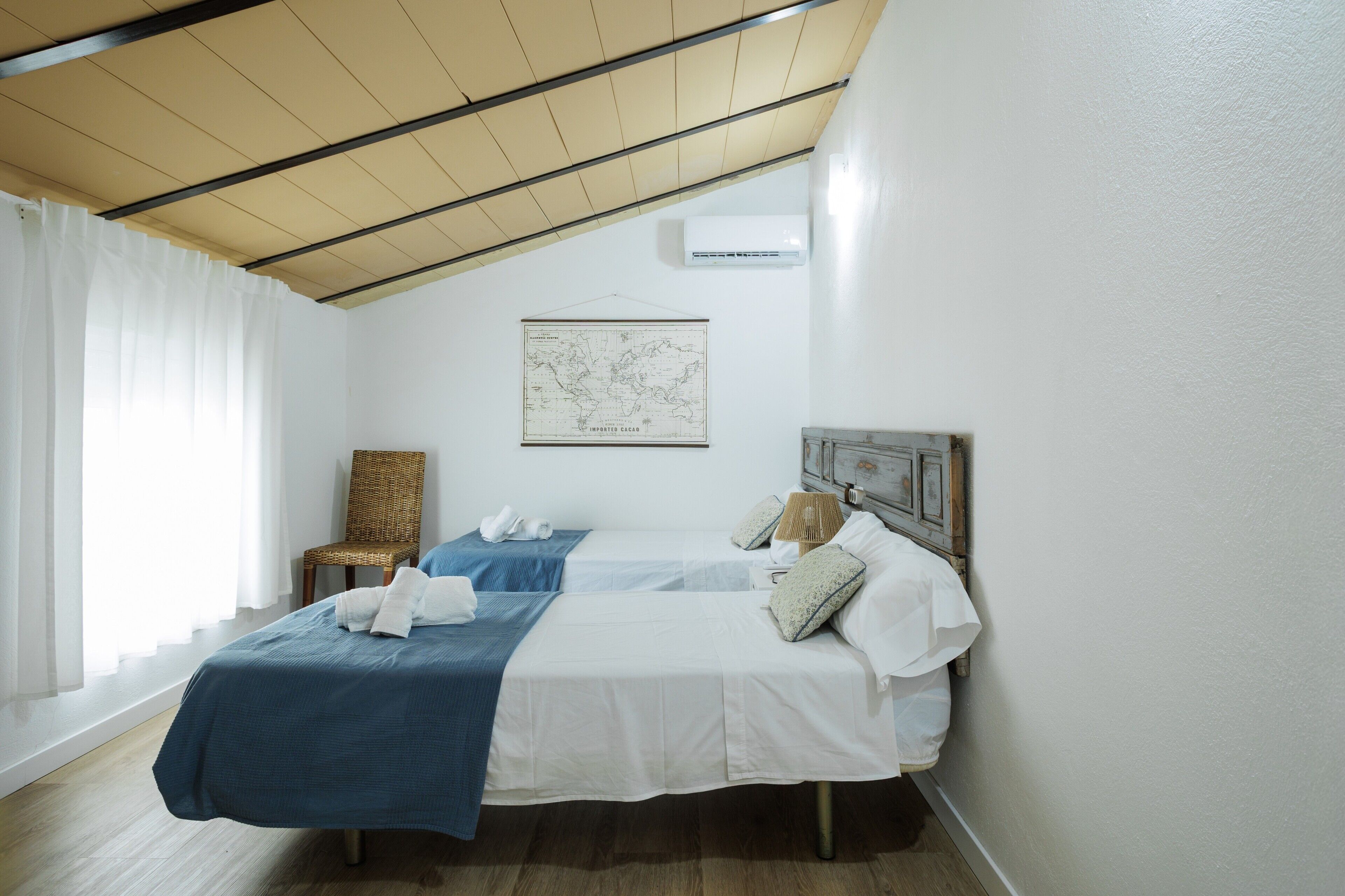 Een slaapkamer met twee bedden, een kaart aan de muur, een rieten stoel en een airconditioning.