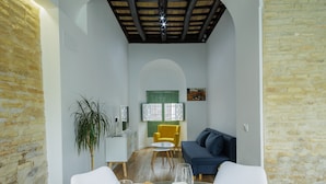 Een kleine kamer met een eettafel gedekt voor twee personen, een bank, een plant en een raam met luiken.