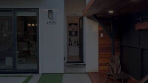 En moderne bygning med to etager, fladt tag, tydelig indgang og et lille udendørs siddeområde med stole.