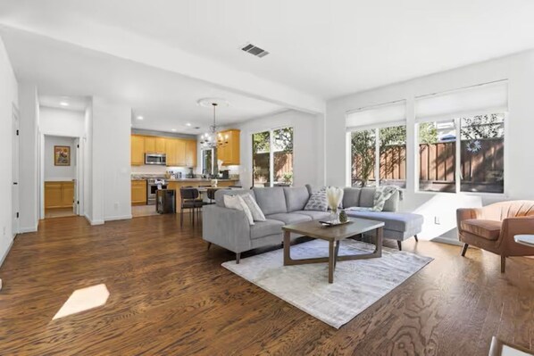 A spacious living area with hardwood flooring, a gray sofa, a coffee table, and a kitchen in the background.