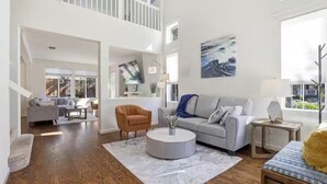 A spacious living area with a high ceiling, a staircase, and a large window.
