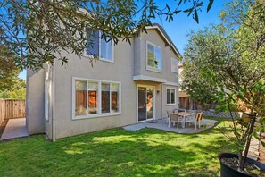 A two-story house with a patio, a small garden, and a tree.