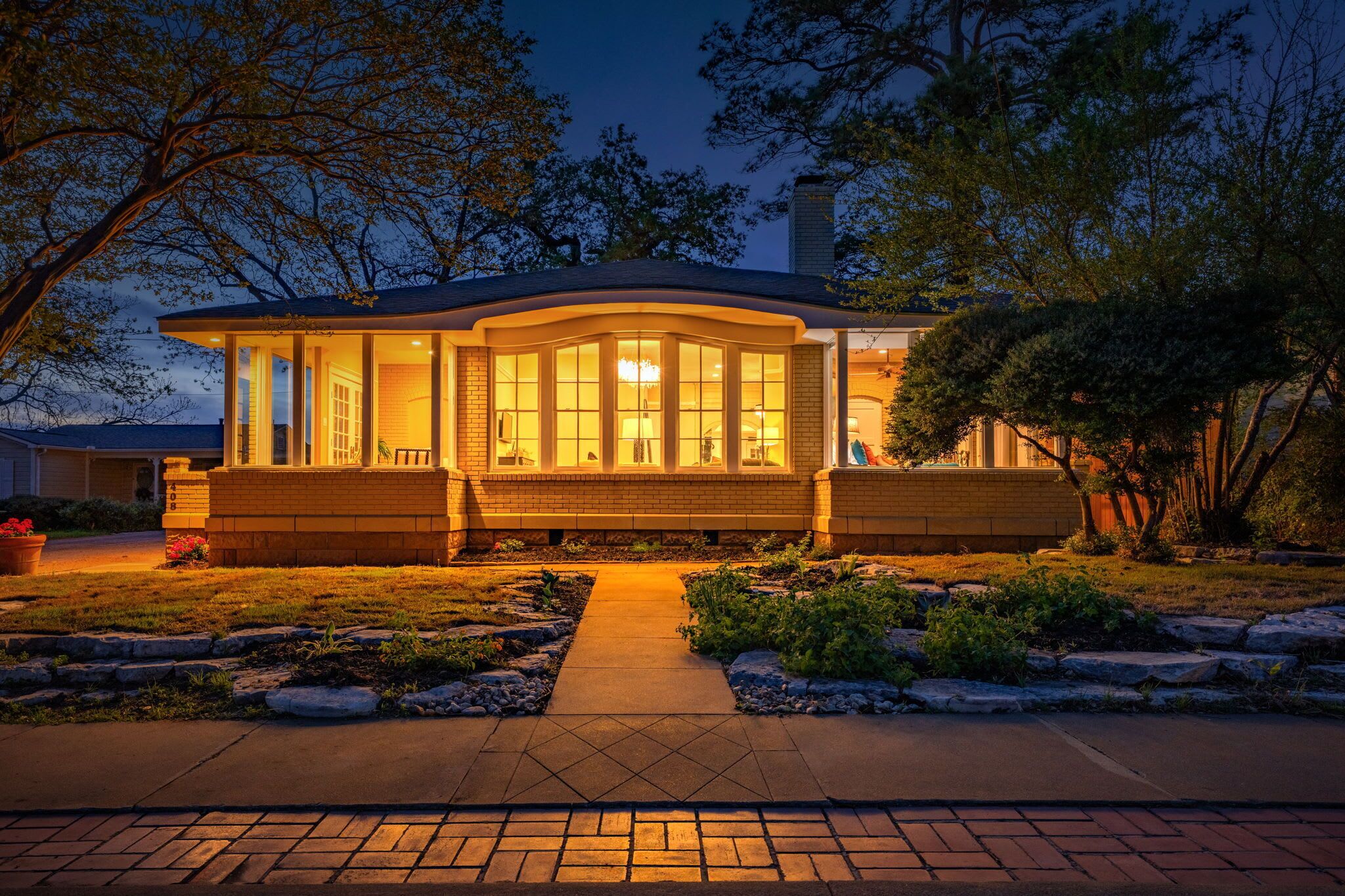 A house with a covered porch, a brick exterior, and a pathway leading to the entrance.