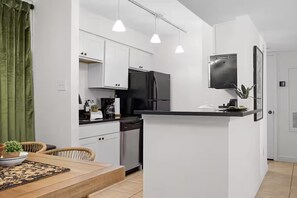 A modern kitchen with white cabinets, a black refrigerator, a dishwasher, and pendant lighting.
