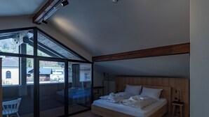 Un dormitorio con un amplio ventanal corredera, una cama con ropa de cama blanca, un cabecero de madera y una mesita de noche pequeña.
