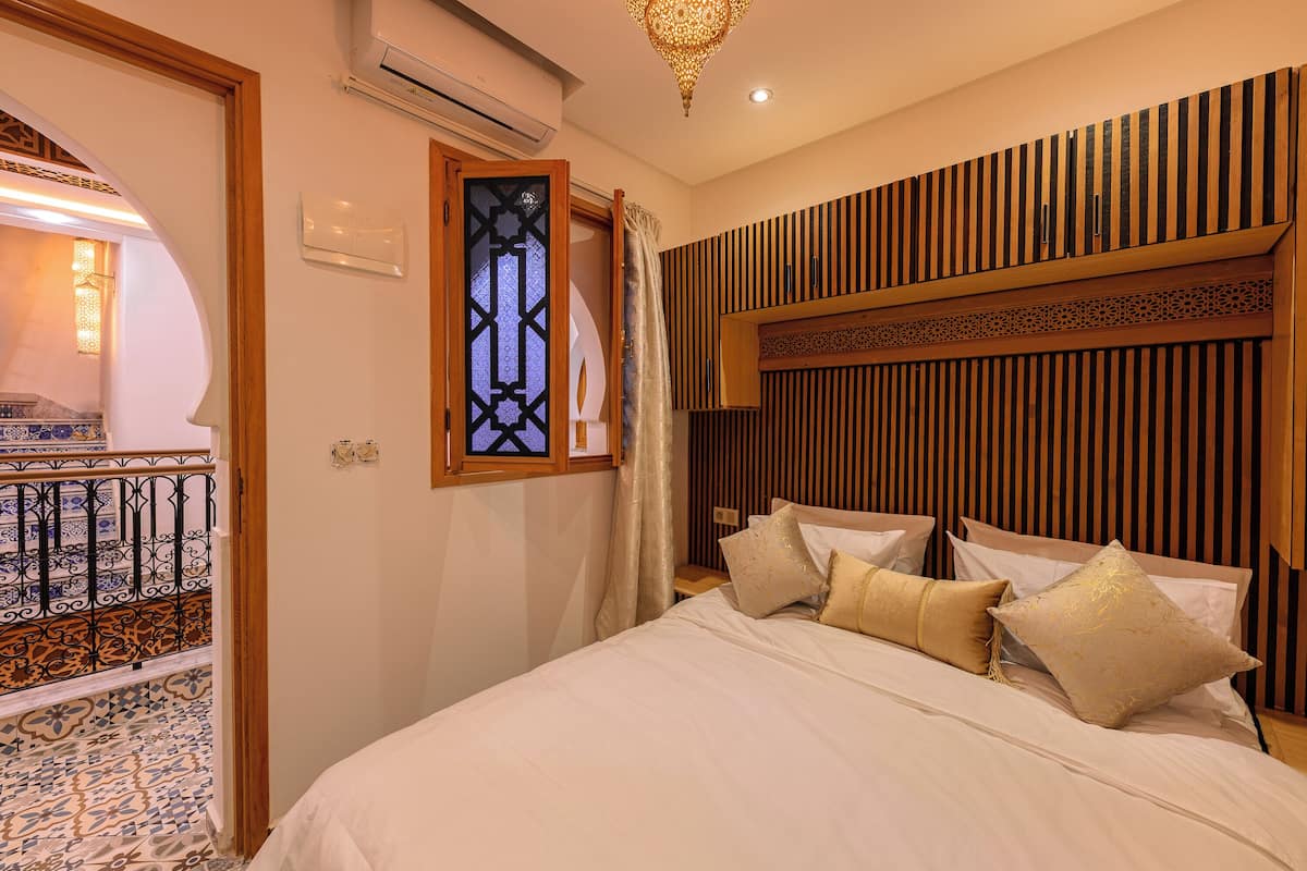 A hotel room with a bed, a decorative wall panel, a window with a curtain, and a patterned floor.